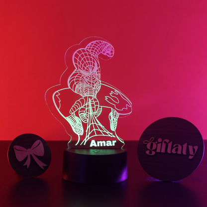 A personalized 3D optical illusion night light featuring Spider-Man holding a donut, with the name 'Amar' engraved on the base. The night light is illuminated with a green-to-pink gradient light, flanked by two round wooden gift box lids engraved with 'giftaty' and a bow, set against a vibrant red and pink gradient background.